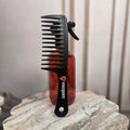 Tresspoint wide-tooth detangling comb in black with the Tresspoint logo on the handle, standing on a marble surface