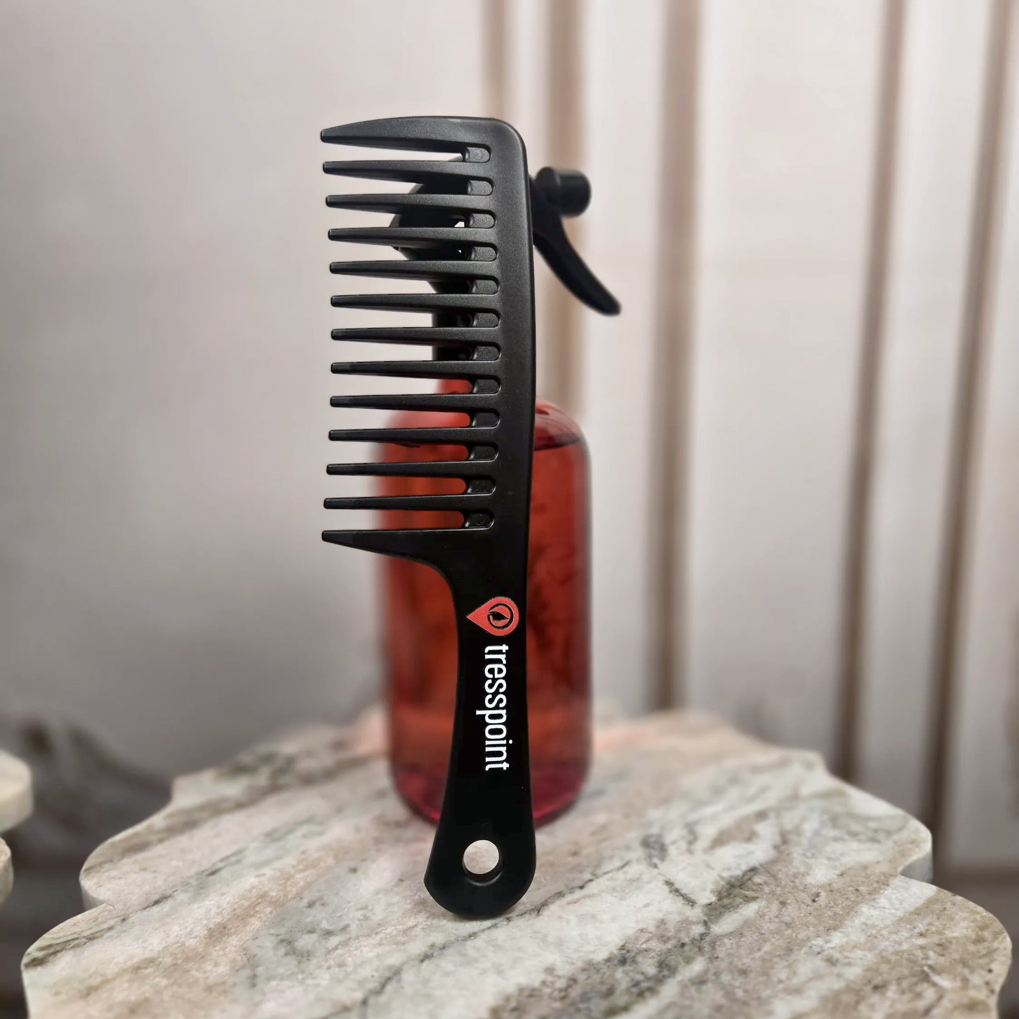 Tresspoint wide-tooth detangling comb in black with the Tresspoint logo on the handle, standing on a marble surface